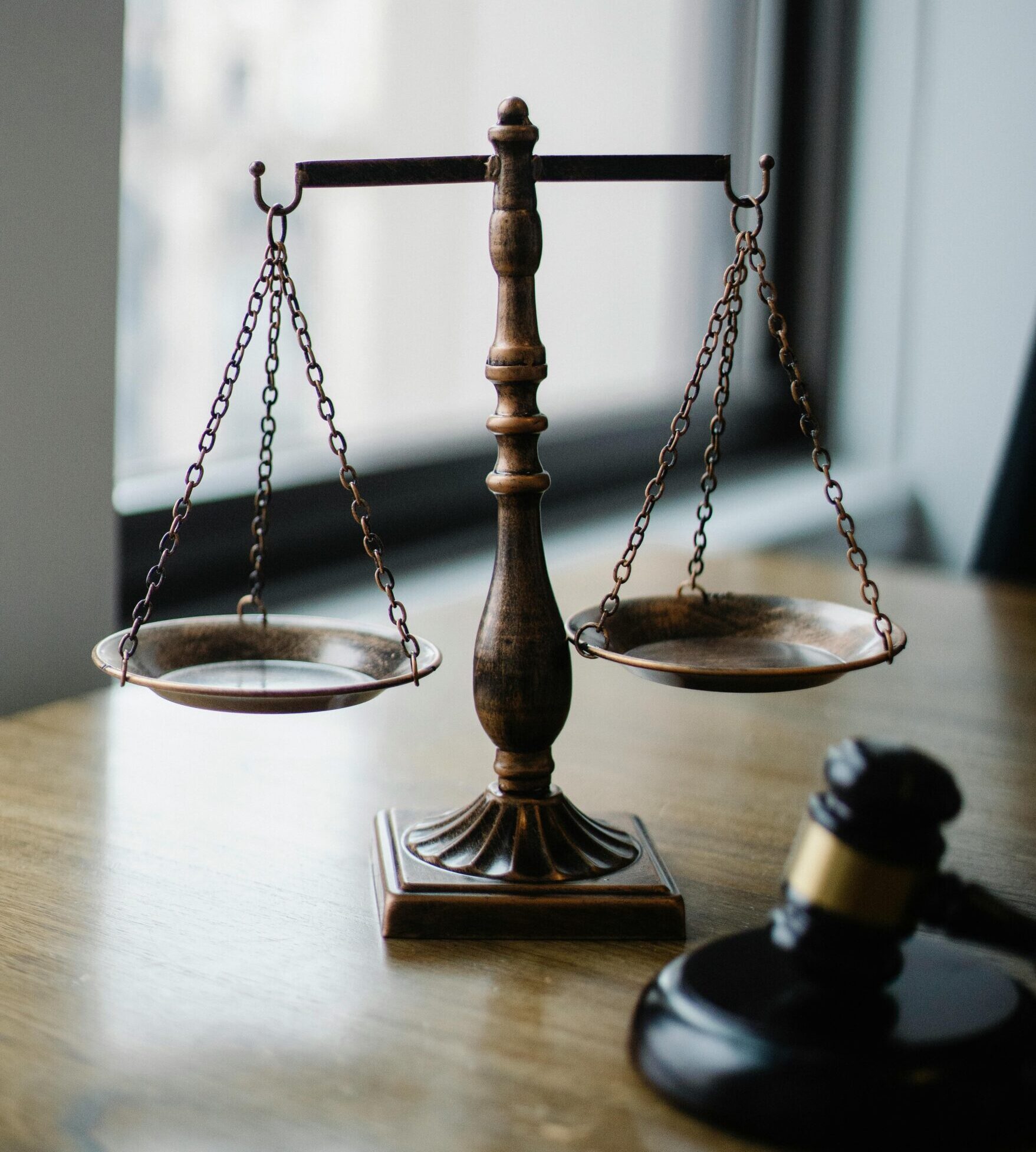 Decorative judgement scale and gavel placed on desk in light lawyer office against window.