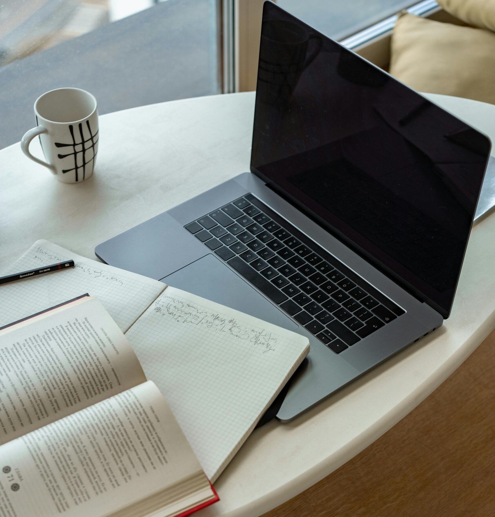 Open laptop and notebooks with handwritten notes and coffee cup on a light desk.